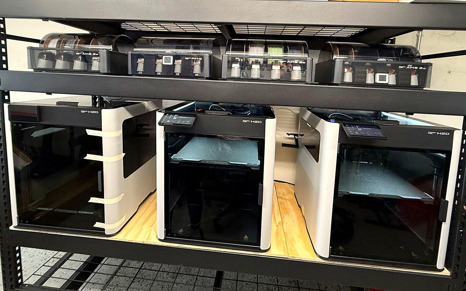 The 3D Print Live workshop: three Bambu Lab H2D printers with automatic multi-material filament units on the shelf above